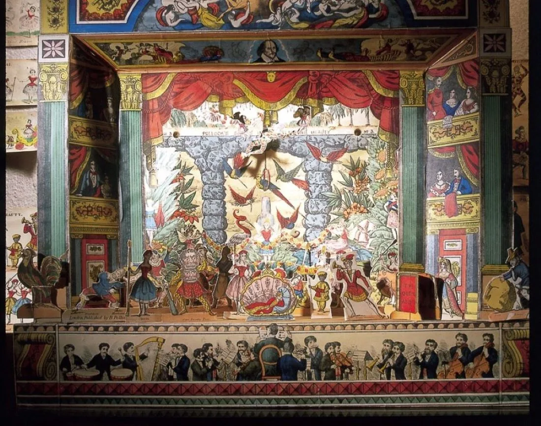 An ornate antique toy theatre with painted scenery, curtains and rows of paper figures on its stage.
