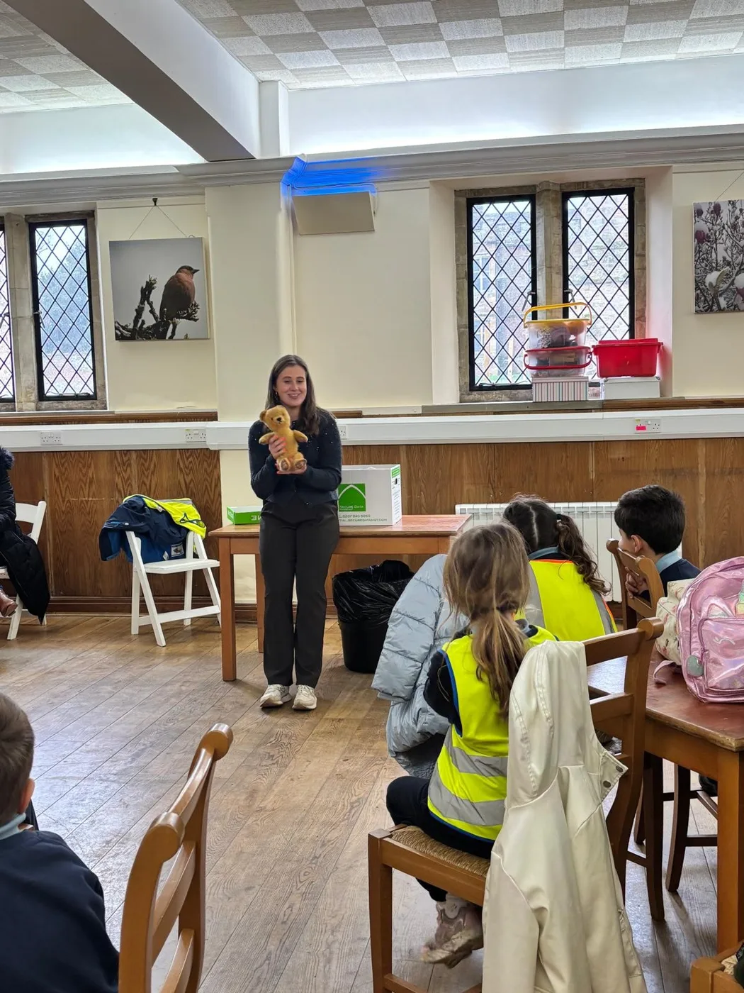 A session leader holds up a teddy bear in front of seated pupils wearing high-visibility vests.