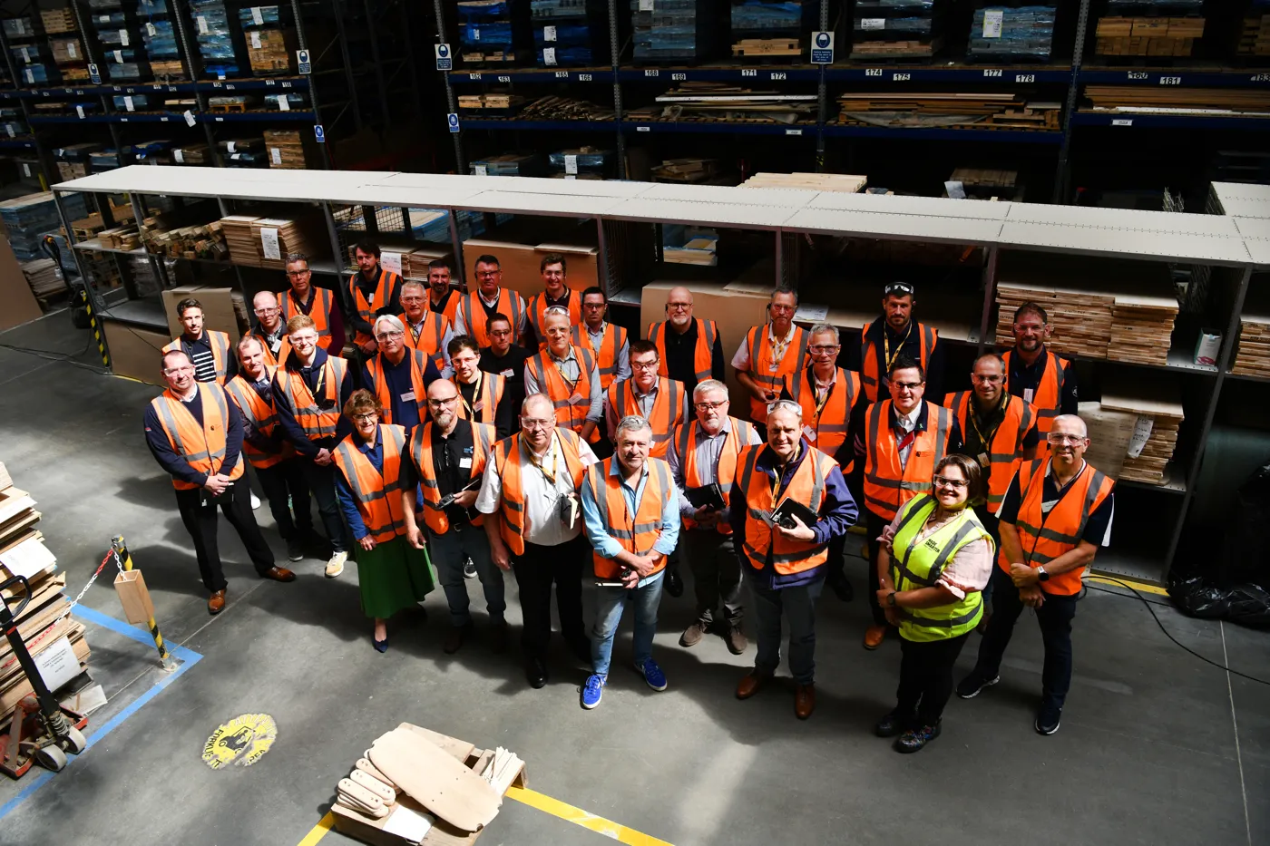 About 30 people in high-visibility vests pose for a group photograph in an Ercol warehouse, seen from above.